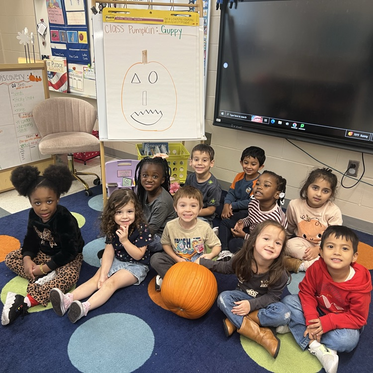 Students posing in a classroom with a pumpkin at the center