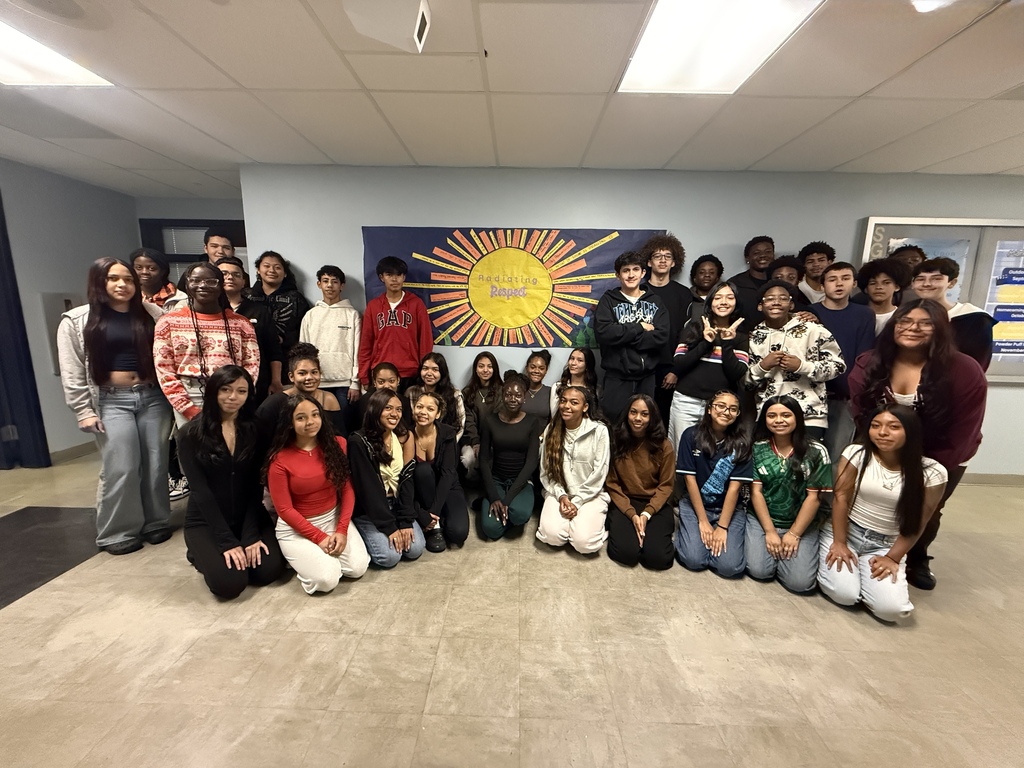 Large group of students posing in front of a sun bulletin board display