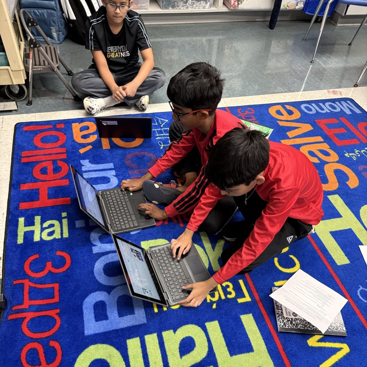 Students working together on carpet on computers