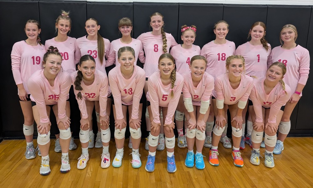 two rows of volleyball players squatting or standing and wearing pink shirts for cancer awareness