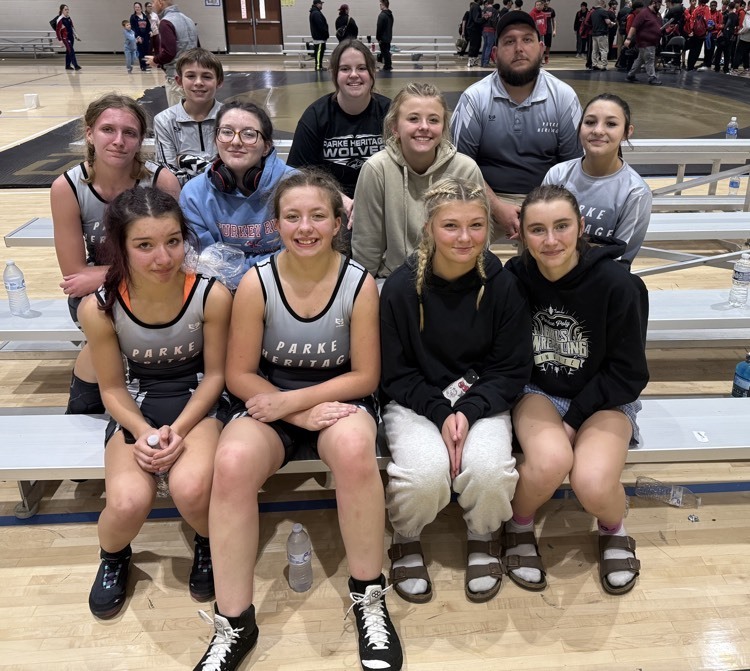 three rows of girl wrestlers and coach sitting on bleachers