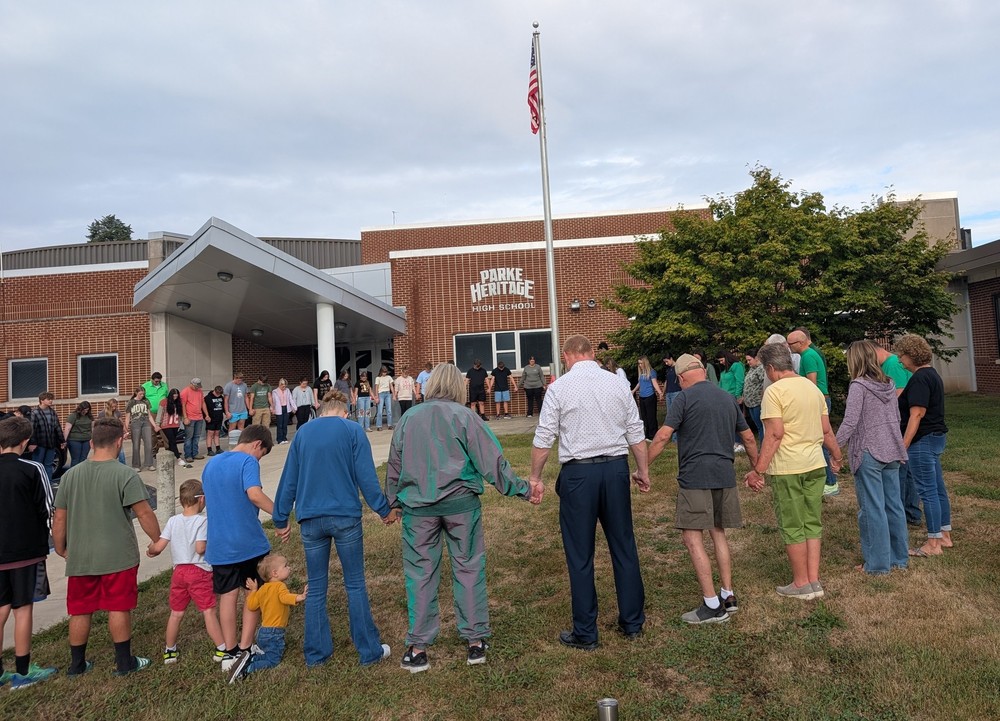 students and adults standing in a circle and holding hands around the flag pole for a time of reflection