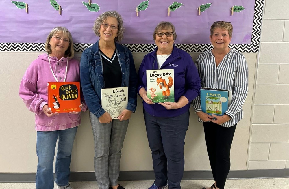 four retired teachers standing in a line holding books