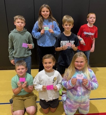 seven students sitting or standing on the gym floor and holding tickets