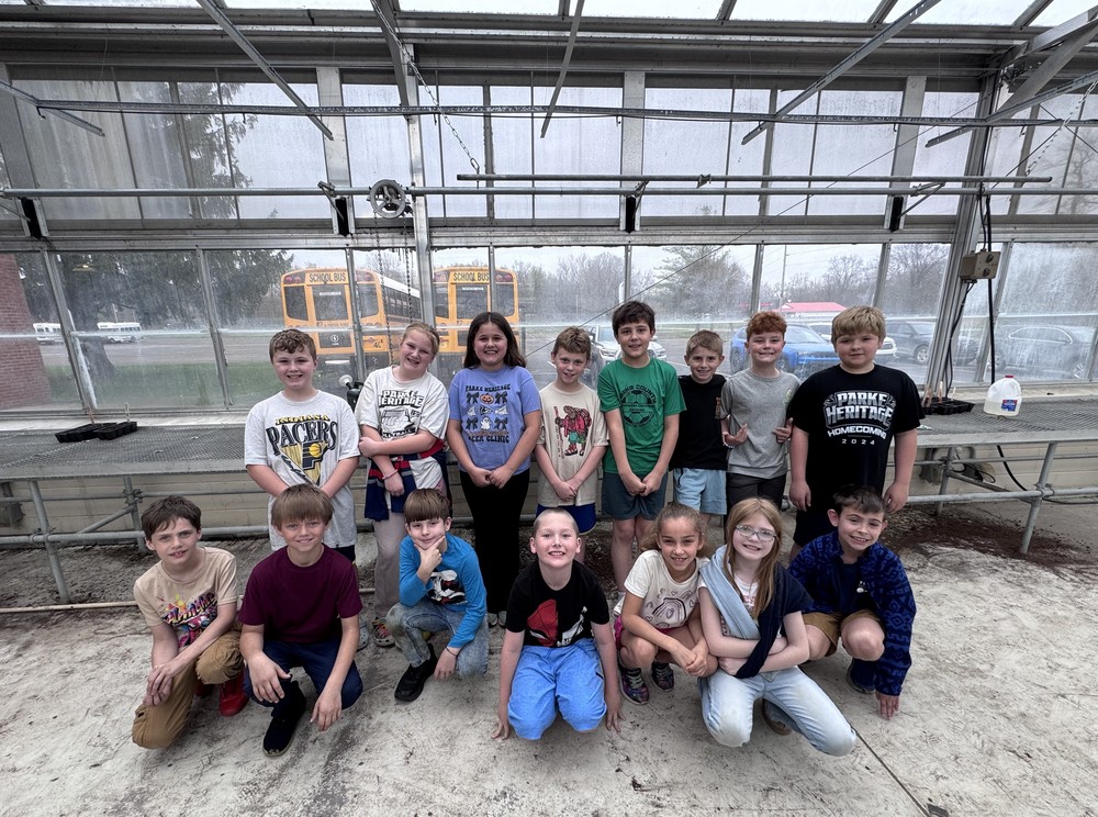 students sitting and standing in rows in a greenhouse