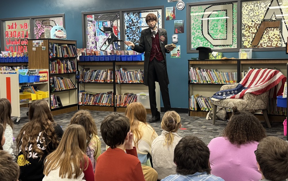 man portraying Abraham Lincoln speaking to students sitting on the floor of the library