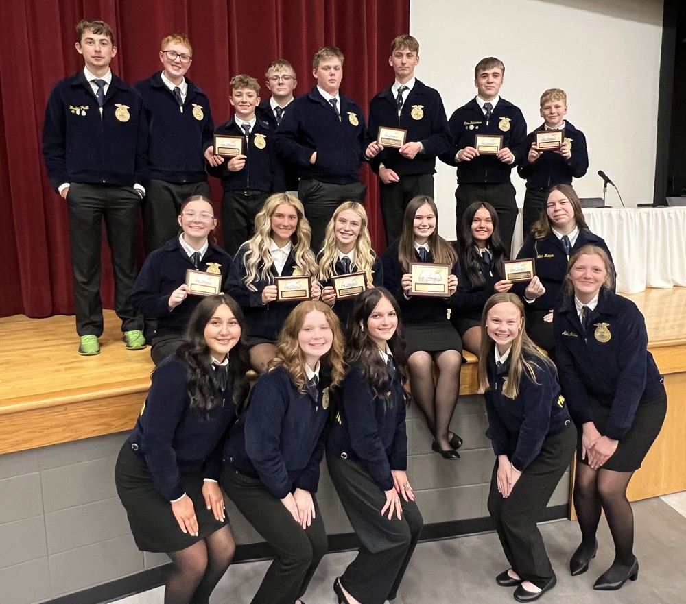 three rows of students kneeling, sitting and standing with some holding plaques