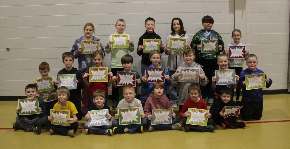 three rows of students sitting, kneeling or standing in the gym while holding certificates