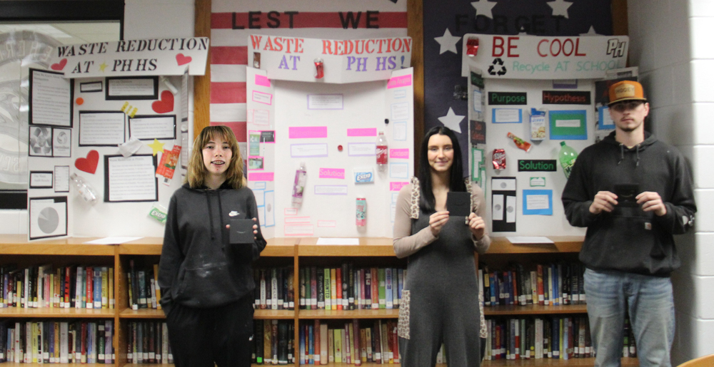 three students holding gift card boxes and standing in front of their display boards