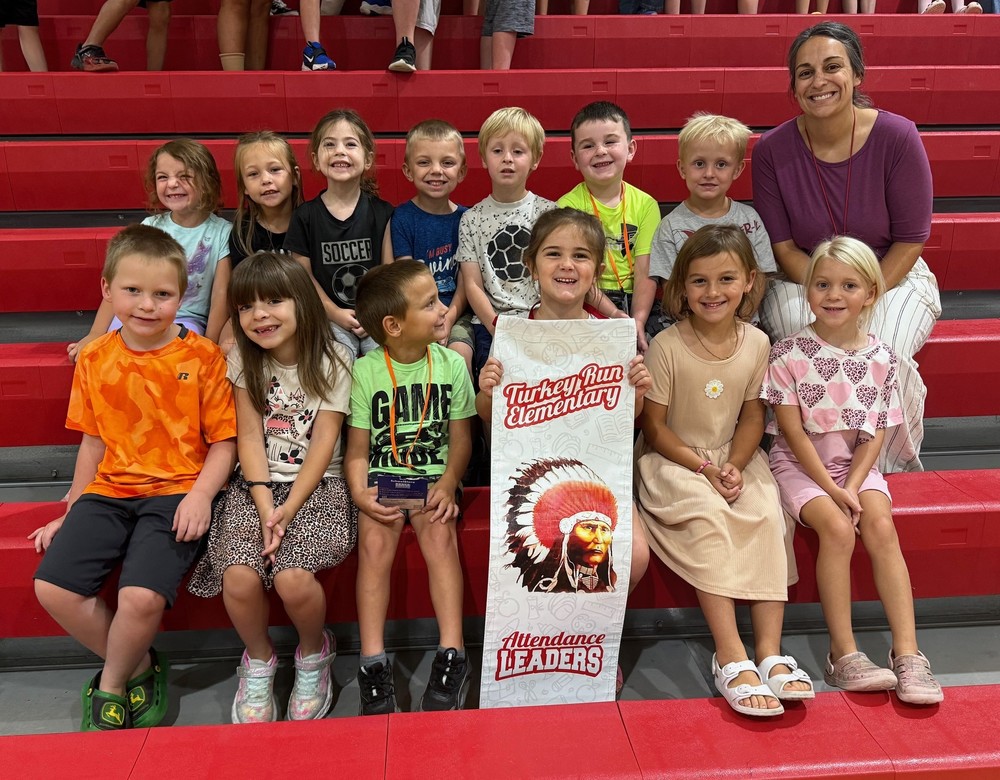 students and a teacher sitting in the bleachers with an attendance leaders banner