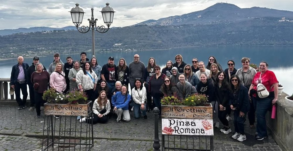 group of students and adults sitting, standing, kneeling in front of some mountains in Italy