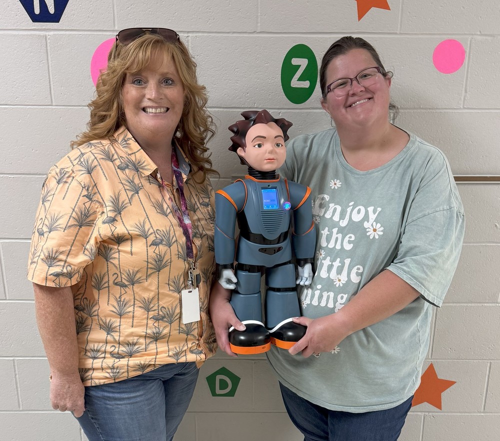 two women standing by a wall with one of them holding a robot