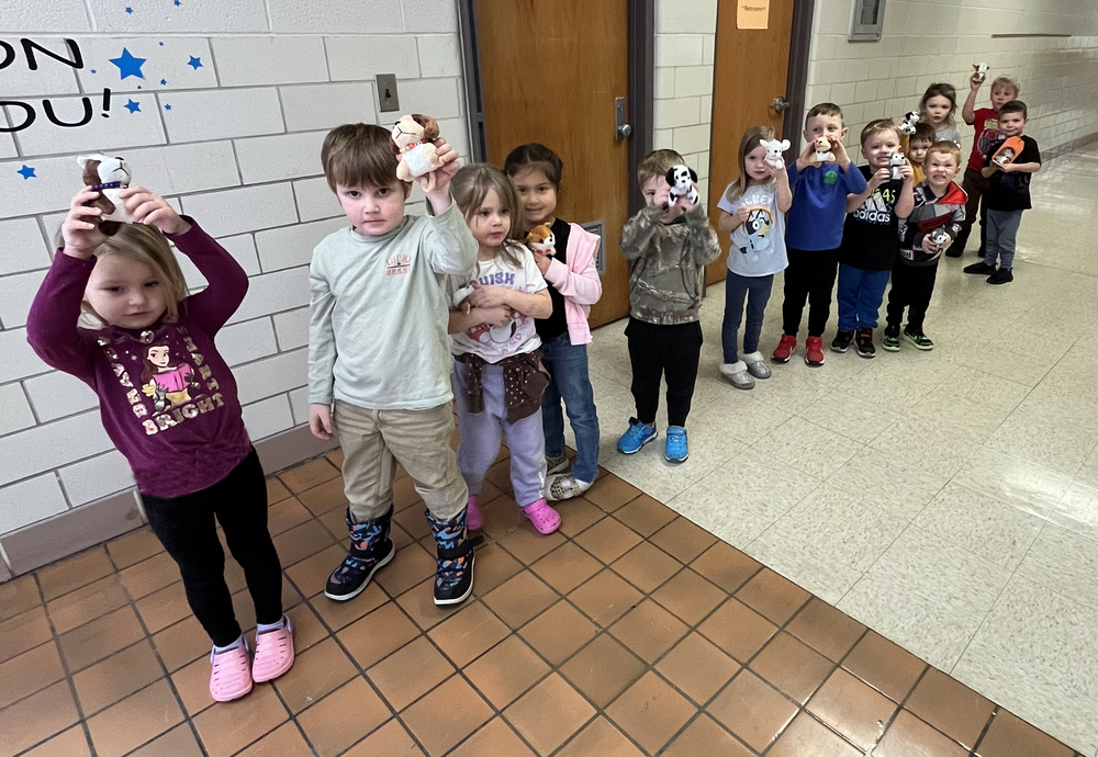 preschool students standing in a line in a school hallway holding plush puppies