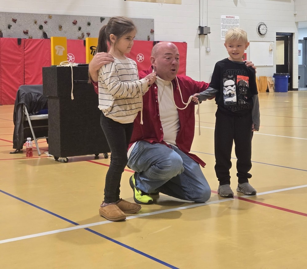 a man kneeling between two students who are holding a rope