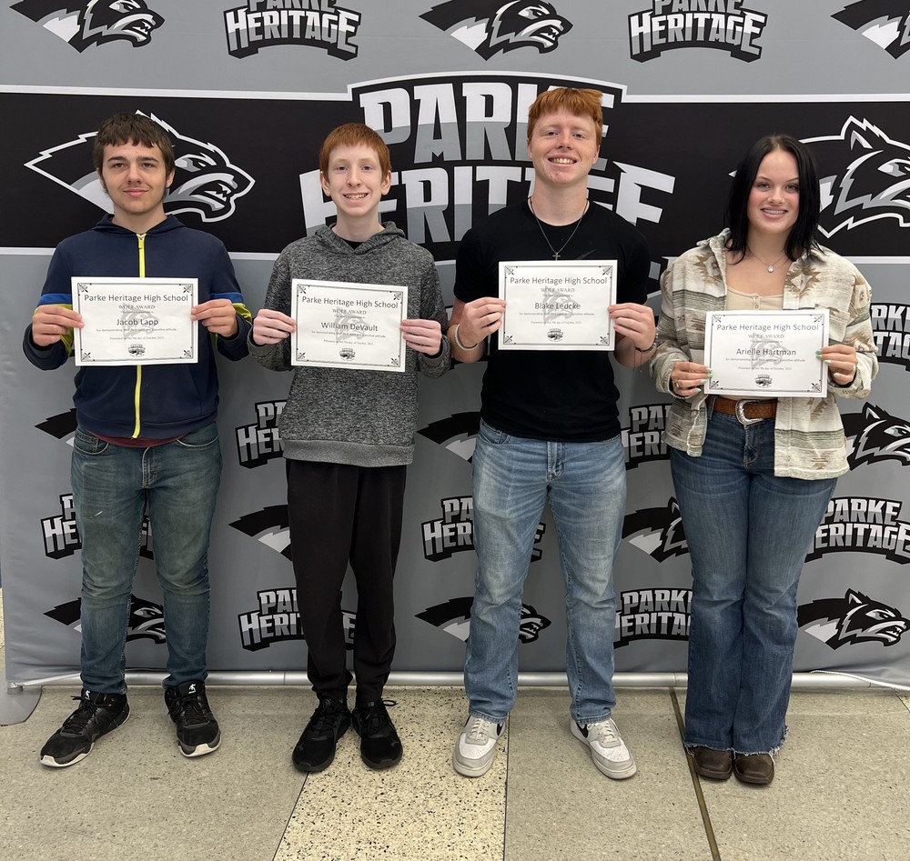 four students standing in front of a backdrop and holding certificates