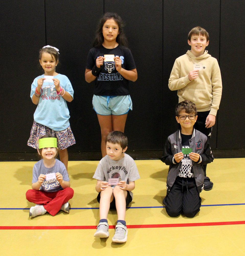 six students sitting and standing on the gym floor holding tickets