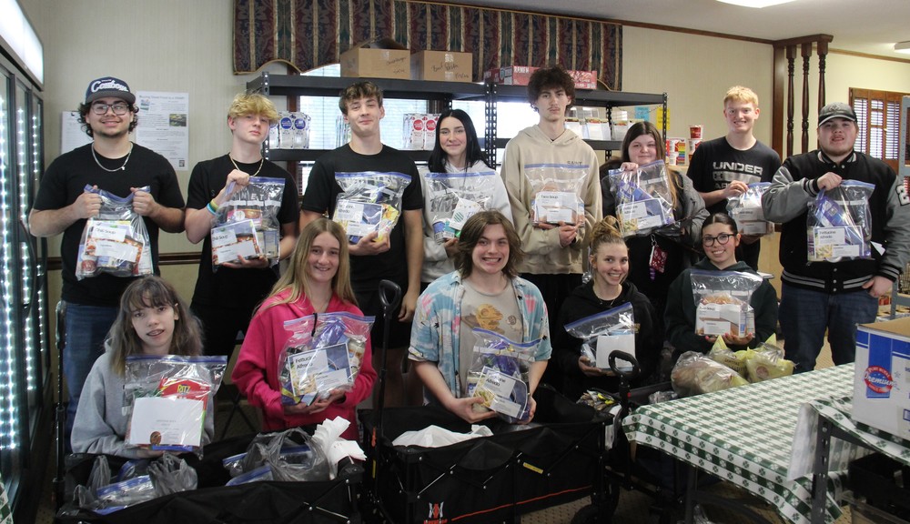 13 students sitting and standing while holding bags of food for the local food pantry
