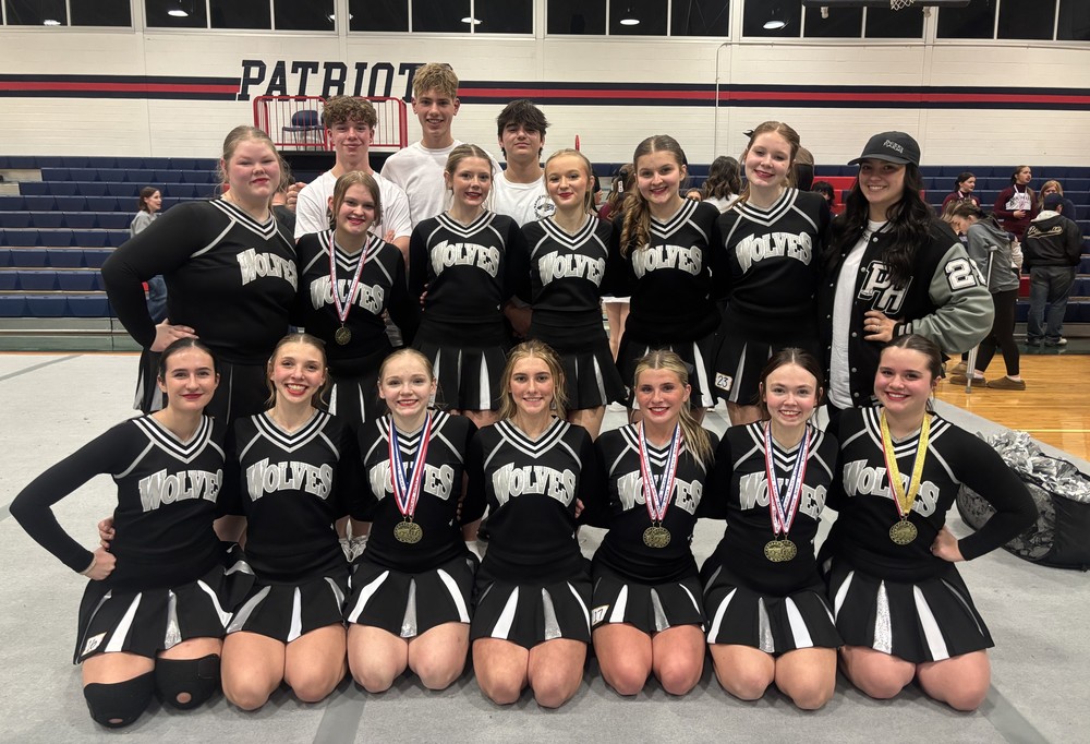 three rows of cheerleaders sitiing and standing in a gym