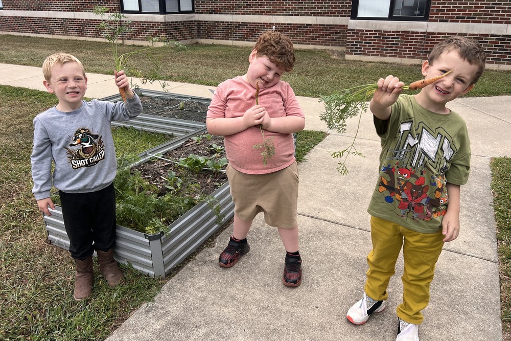 three students holding carrots