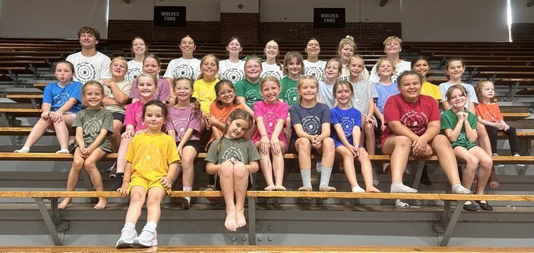 four rows of dance camp participants sitting in the gym bleachers 