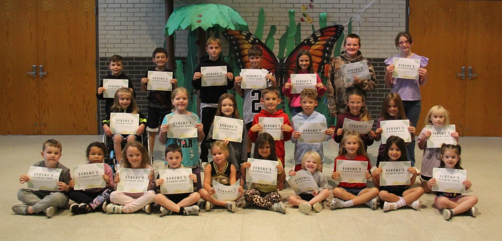 three rows of students sitting, kneeling or standing outside the cafeteria while holding certificates