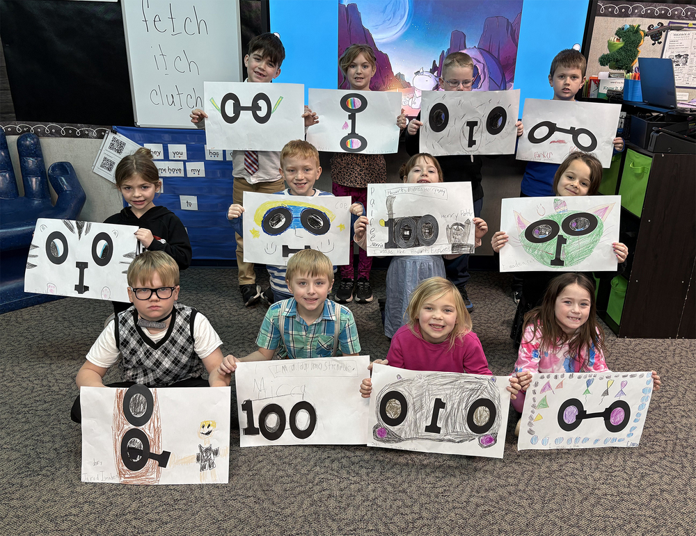 students sitting, kneeling and standing and holding posters with 100 on them