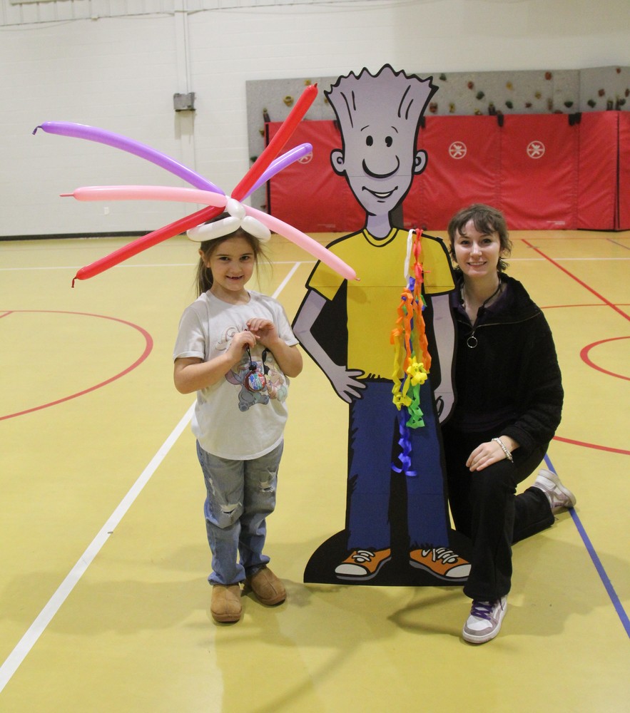 a student wearing a balloon crown, man cardboard cut-out, and woman guest speaker