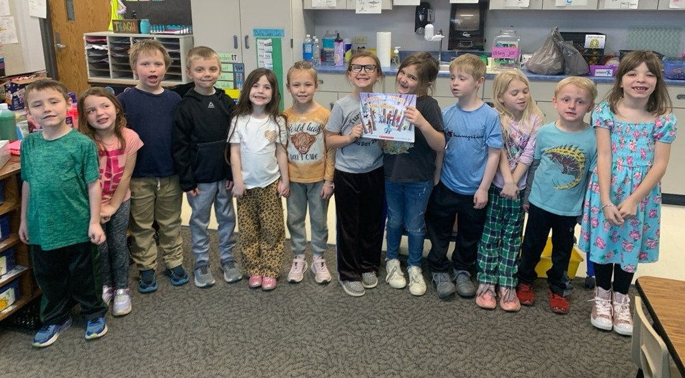 12 students standing in a row with two of them holding a book
