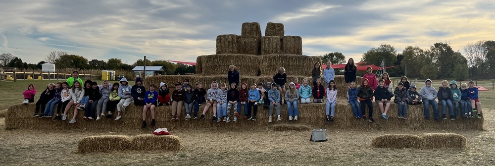 students sitting on hay bales at an apple orchard