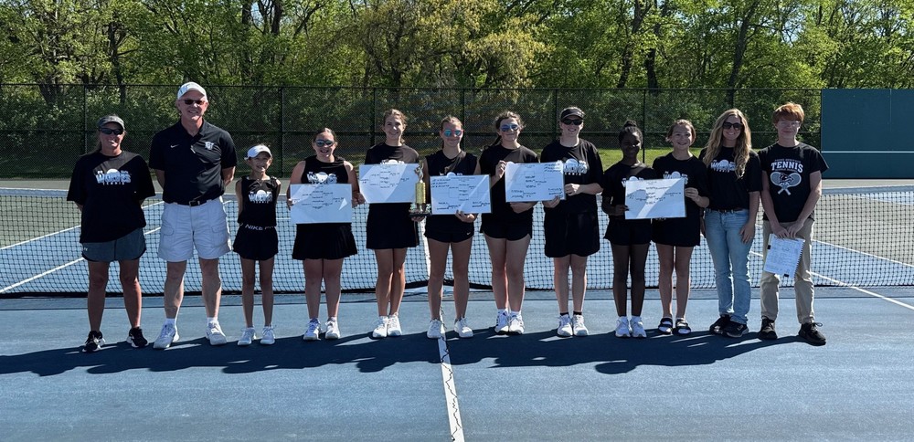 12 people standing on a tennis court with five of them holding tourney cards