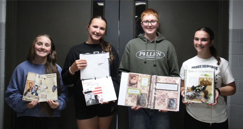 four students standing in a row holding scrapbooks