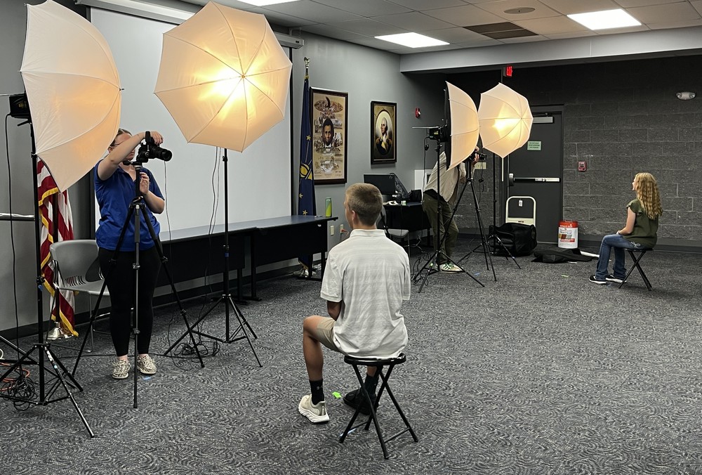 two students sitting on stools while photographers take their school portrait