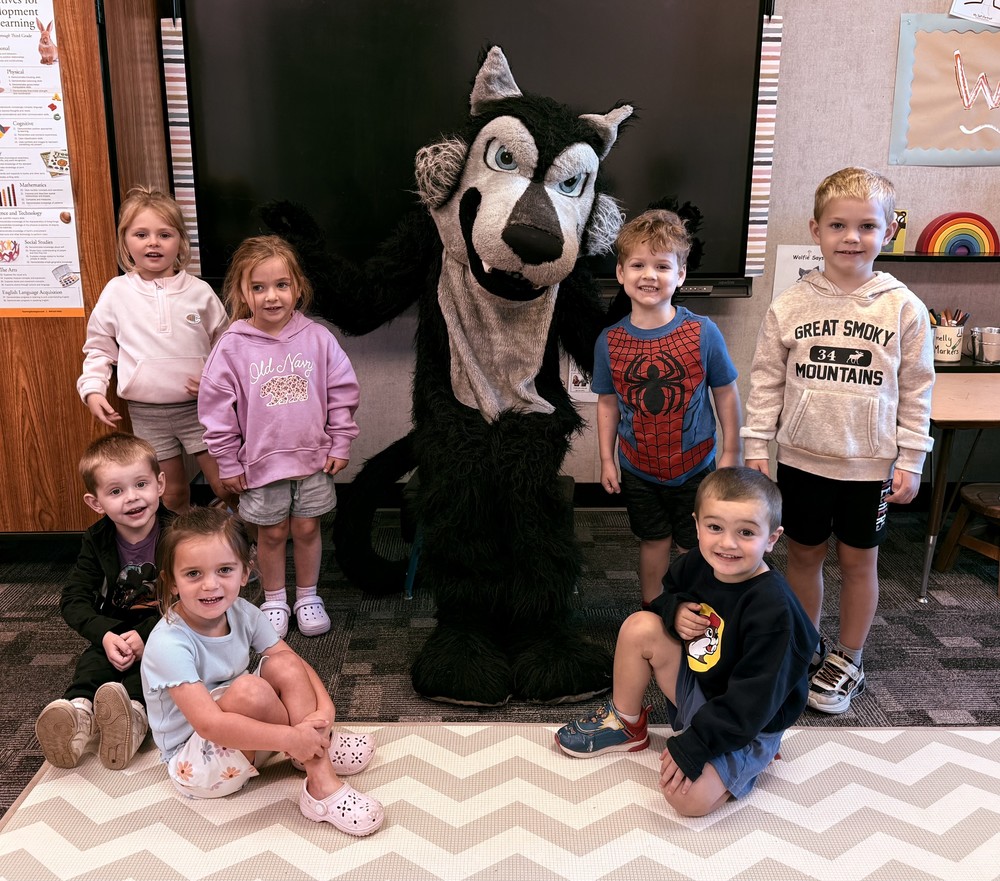 Wolf mascot with seven preschool students gathered around him