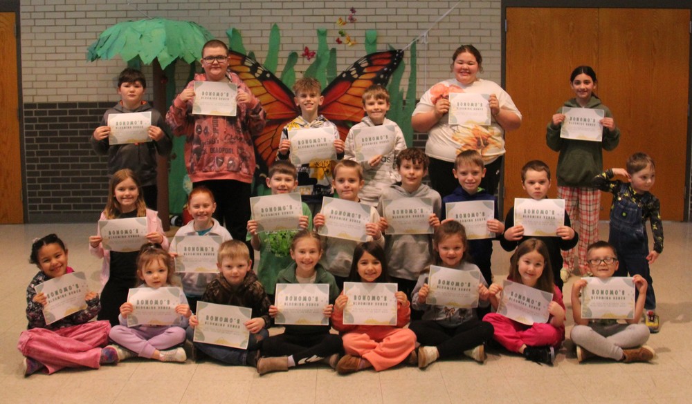 students sitting, kneeling, and standing while holding certificates