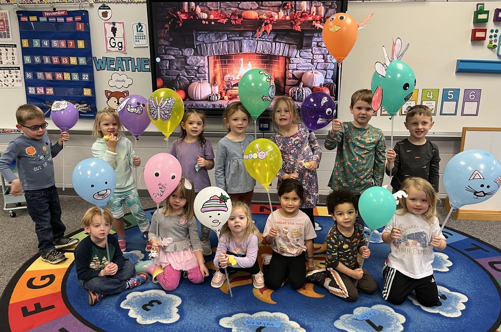 photo of two rows of students sitting or standing while holding balloons