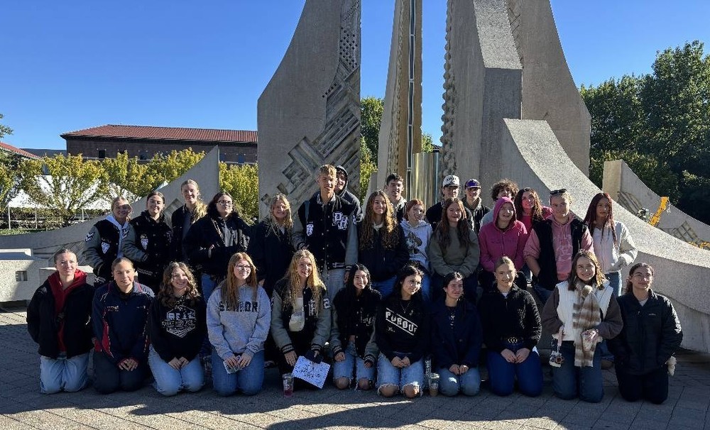 three rows of students sitting or standing in front of Purdue's fountain 