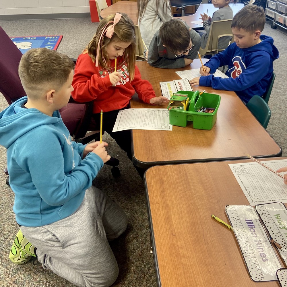 four students sitting at desks writing Santa letters