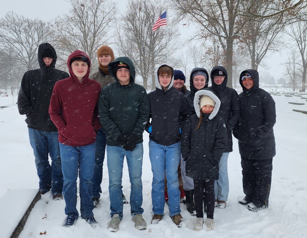 10 students standing in two rows at a cemetery
