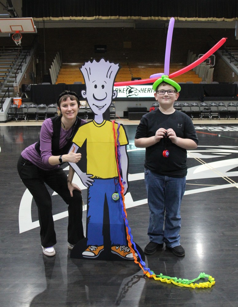 an adult with man cardboard character and a student with balloon hat
