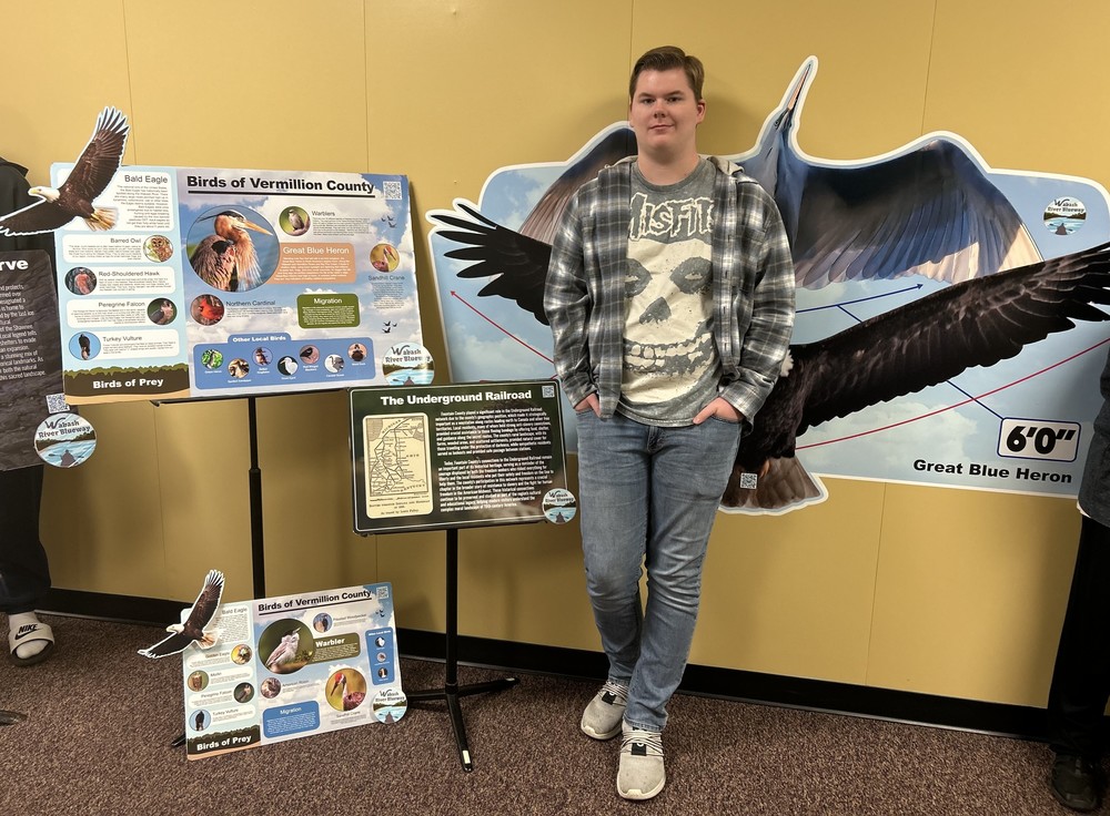 student standing next to graphic design posters he designed