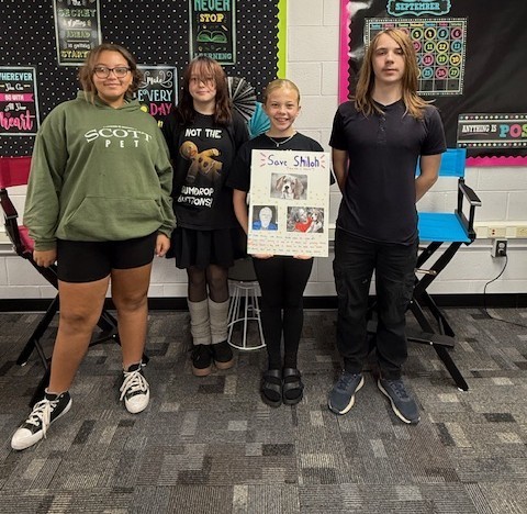 four students standing with one holding a poster