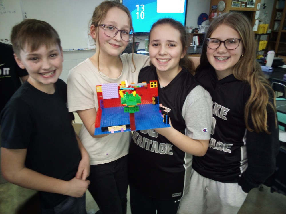 four students standing in a row with two of the students holding a theater set made out of Legos