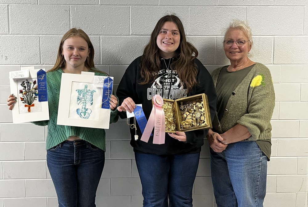 two students and a teacher with the students holding art pieces
