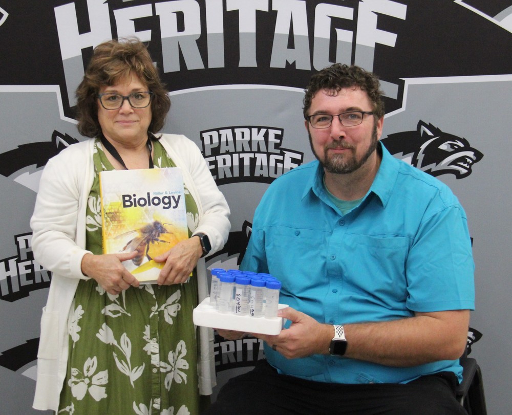 a woman sitting and holding a Biology book and a man sitting and holding a test tube tray