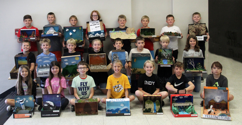 three rows of students sitting, kneeling or standing holding diramas