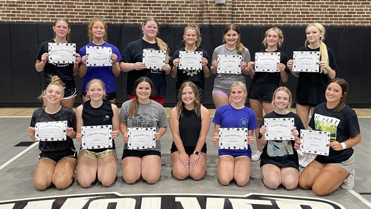 two rows of girls sitting and standing on the gym floor holding certificates