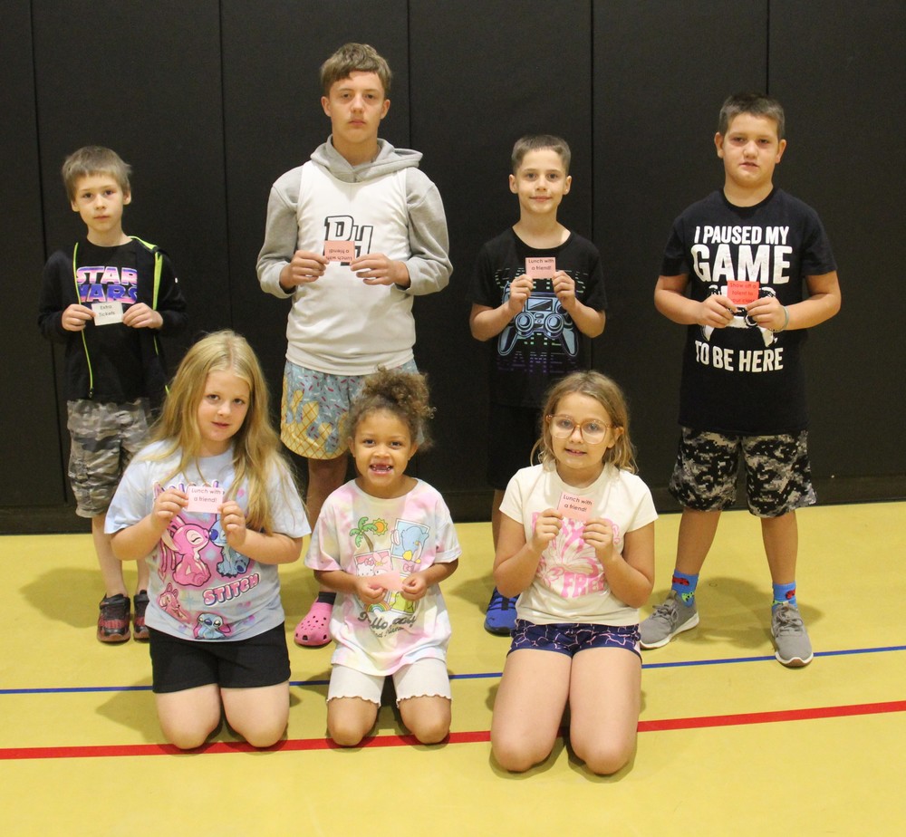 seven students sitting or standing on the gym floor holding tickets