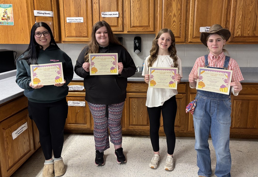 four students standing in a classroom kitchen holding certificates