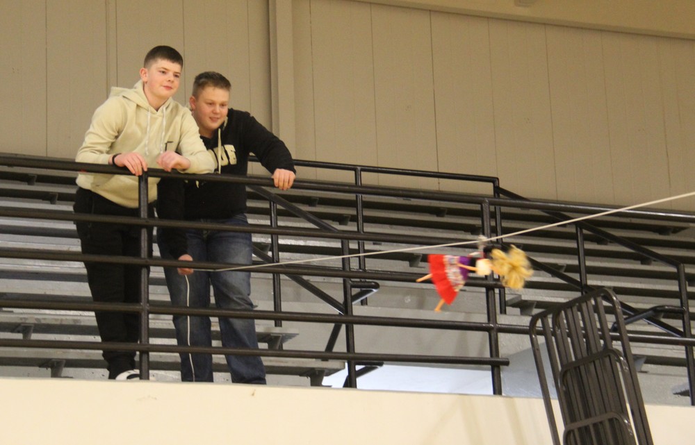 two students watching a Barbie doll on a zipline