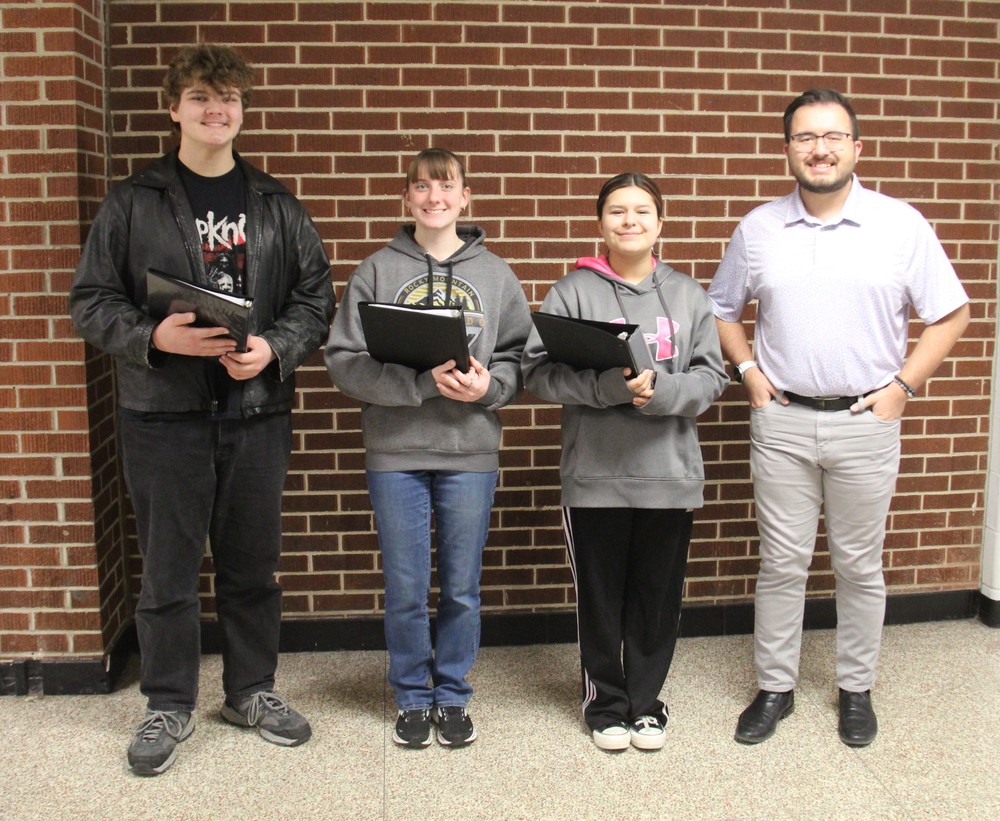 three students holding music binders and their music teacher